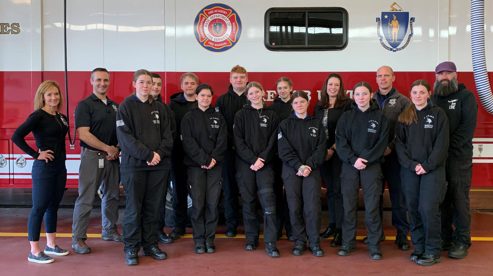 A group of high school students and firefighters in front of a fire engine