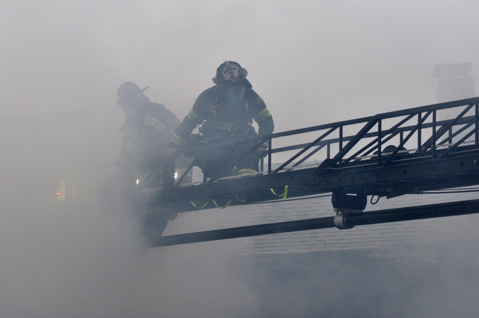 Two firefighters emerging from smoke on an aerial ladder