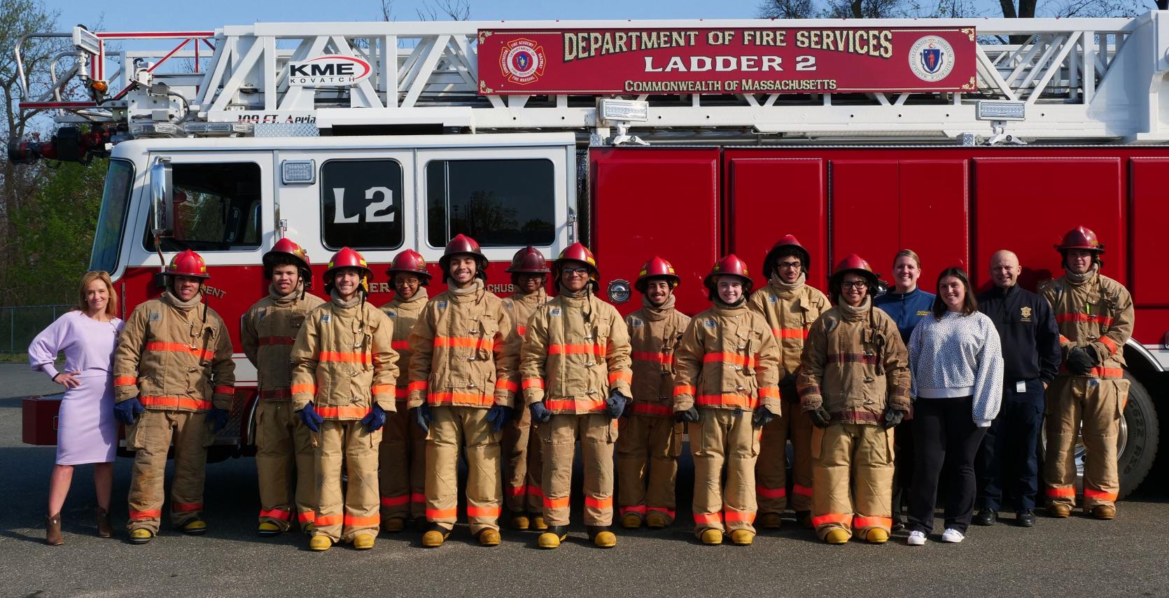 High school students wearing firefighter turnout gear in front of a ladder truck