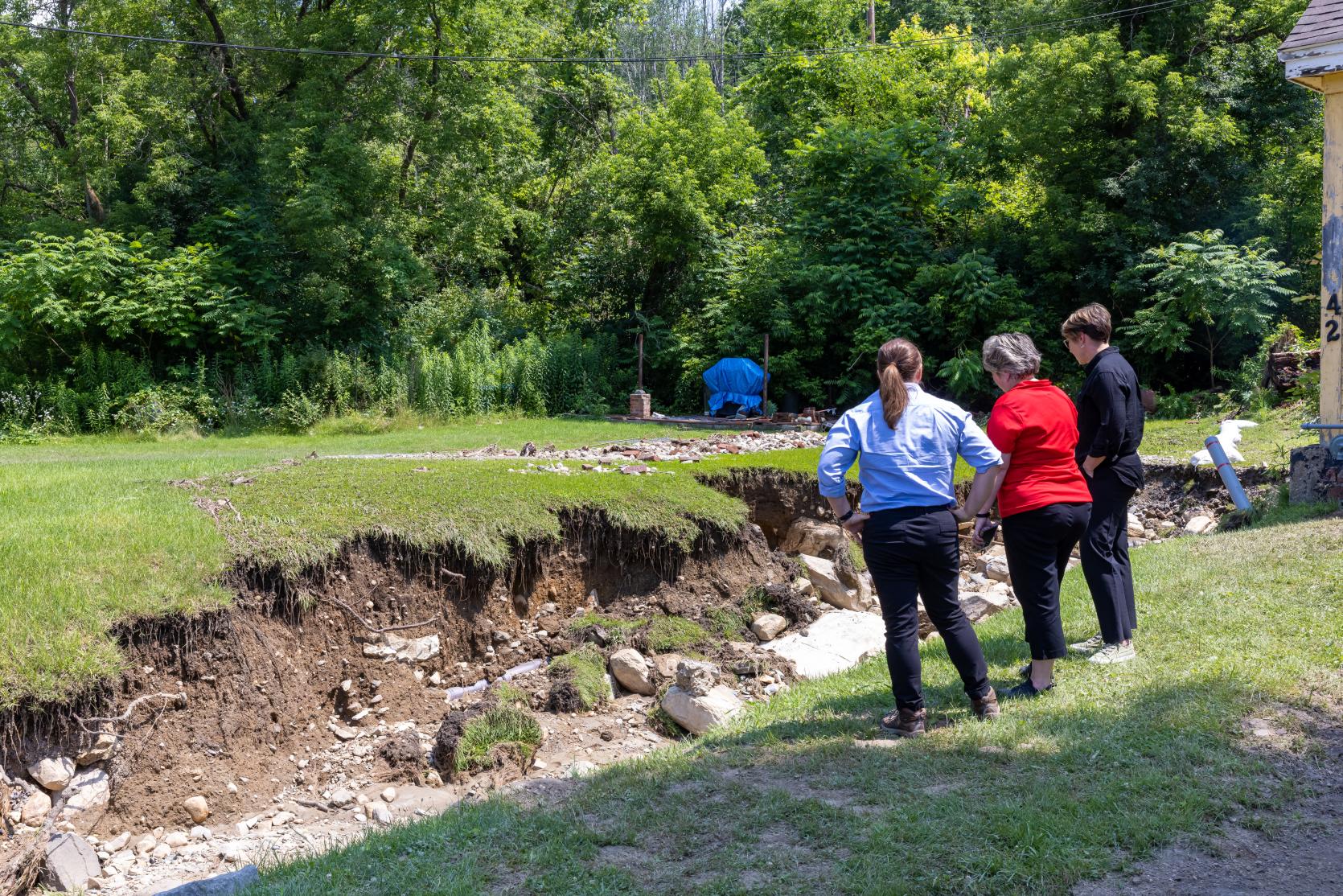 Picture of Dawn Brantley (MEMA), Mayor of North Adams, and Governor Healey looking at damaged yard washed away by flood. 