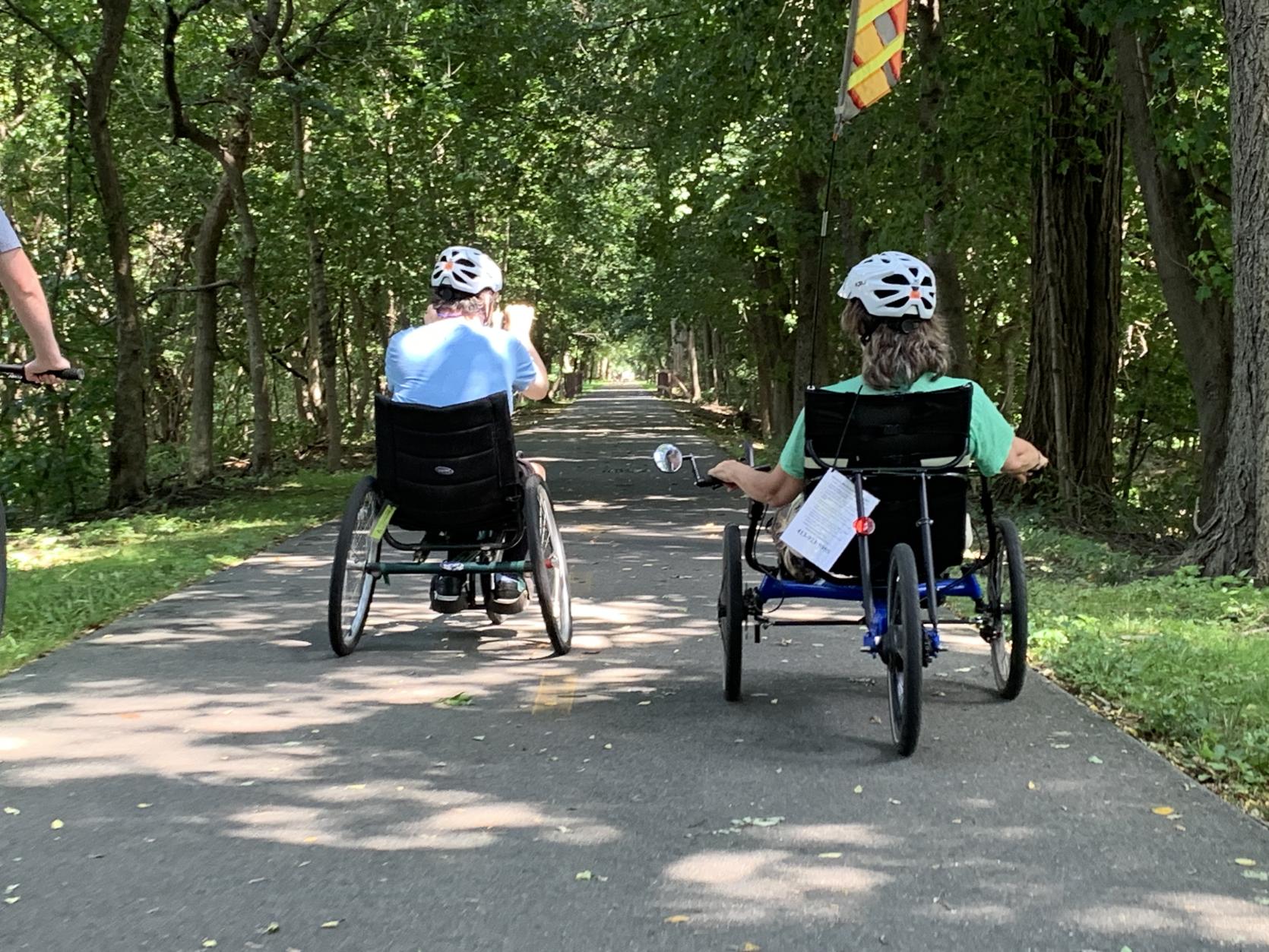 two individuals riding an adaptive cycles on a paved path