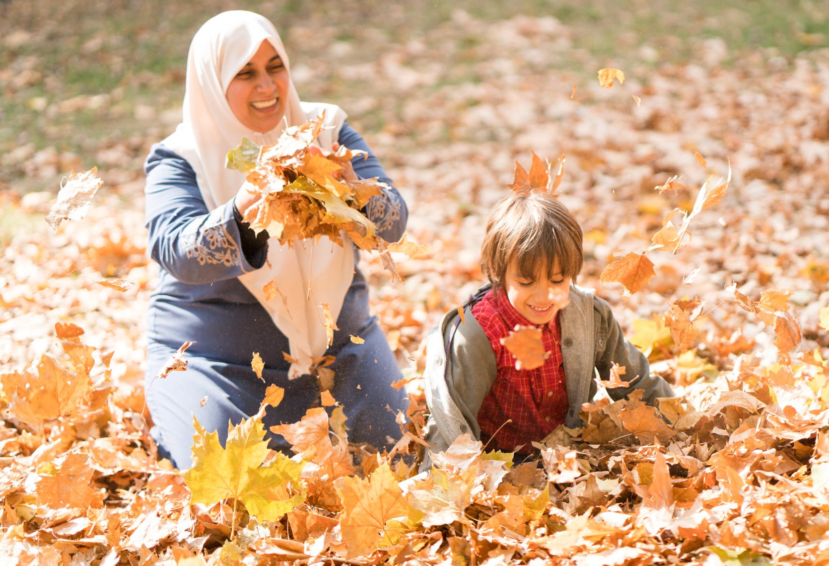 Happy mother and child play in the fall leaves.