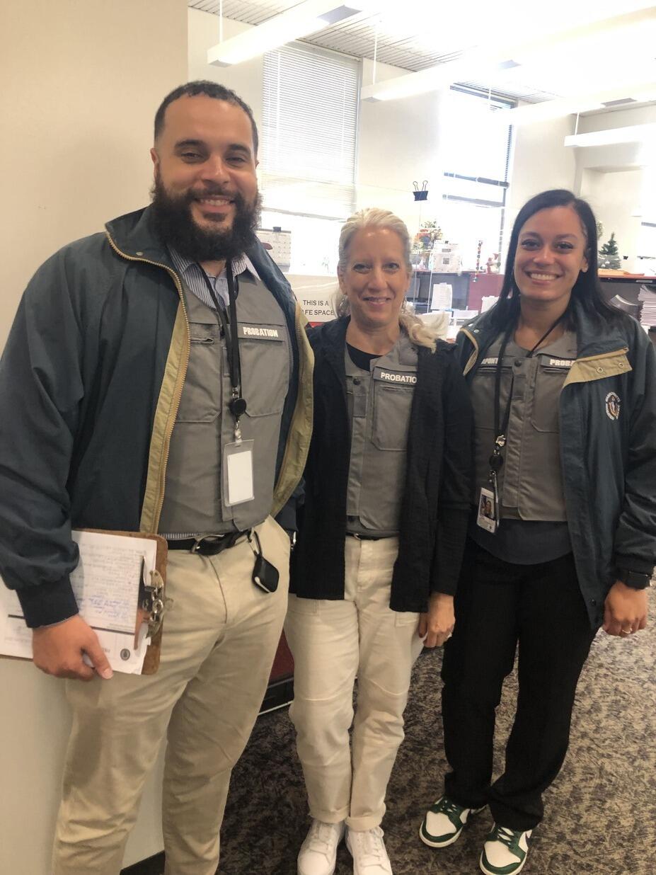 Three people standing in an office wearing matching grey Probation vests.