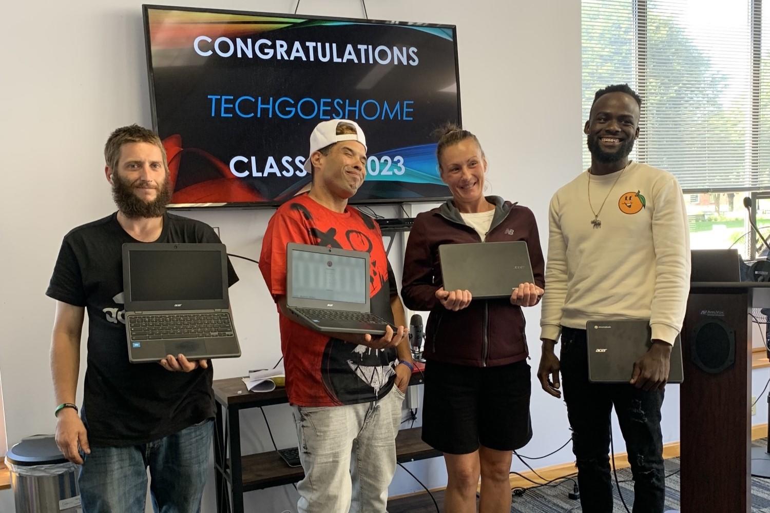 Four TechGoesHome program graduates hold their new laptops. 
