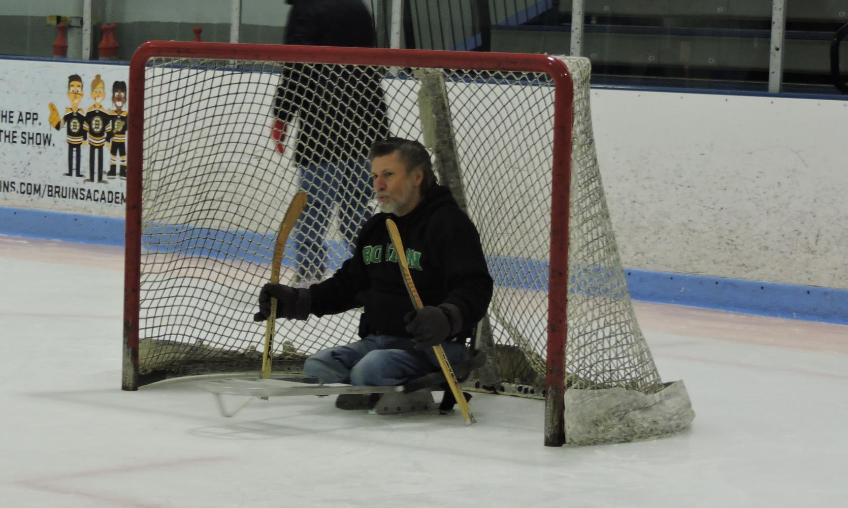 A skater in an ice sled guarding a hockey net.