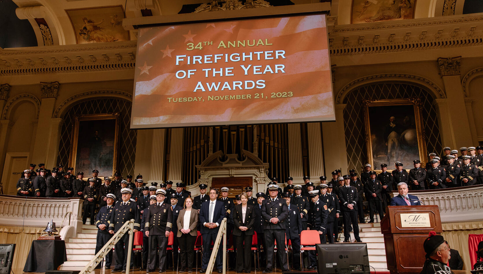 Photo of state officials and firefighters in dress uniforms on a stage