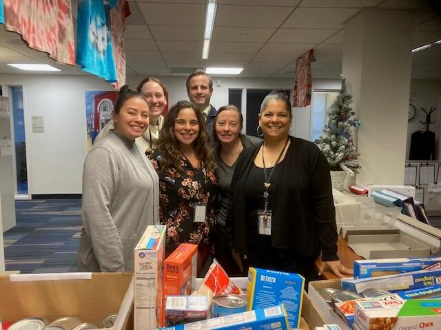 A group of six people standing behind a table full of food donations
