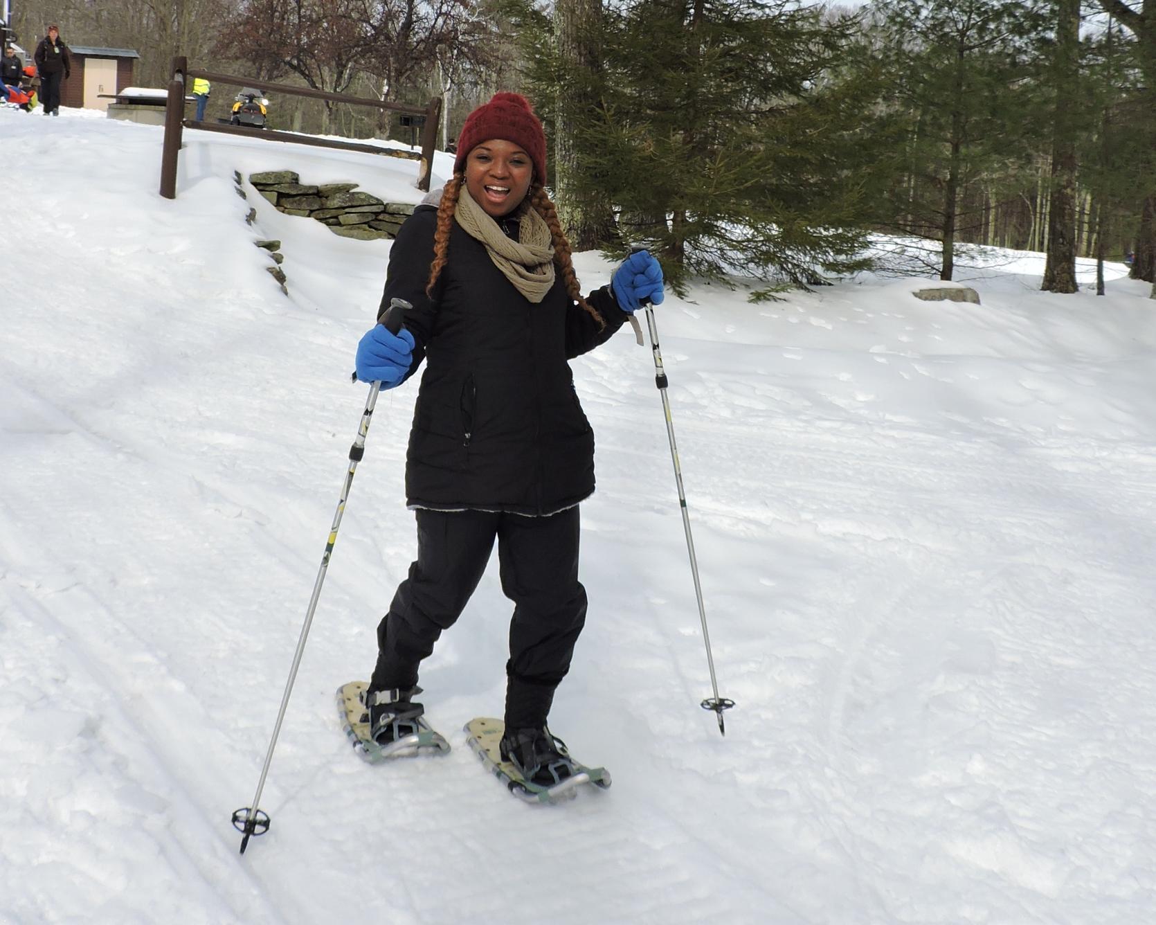 A smiling snowshoer using ski poles.