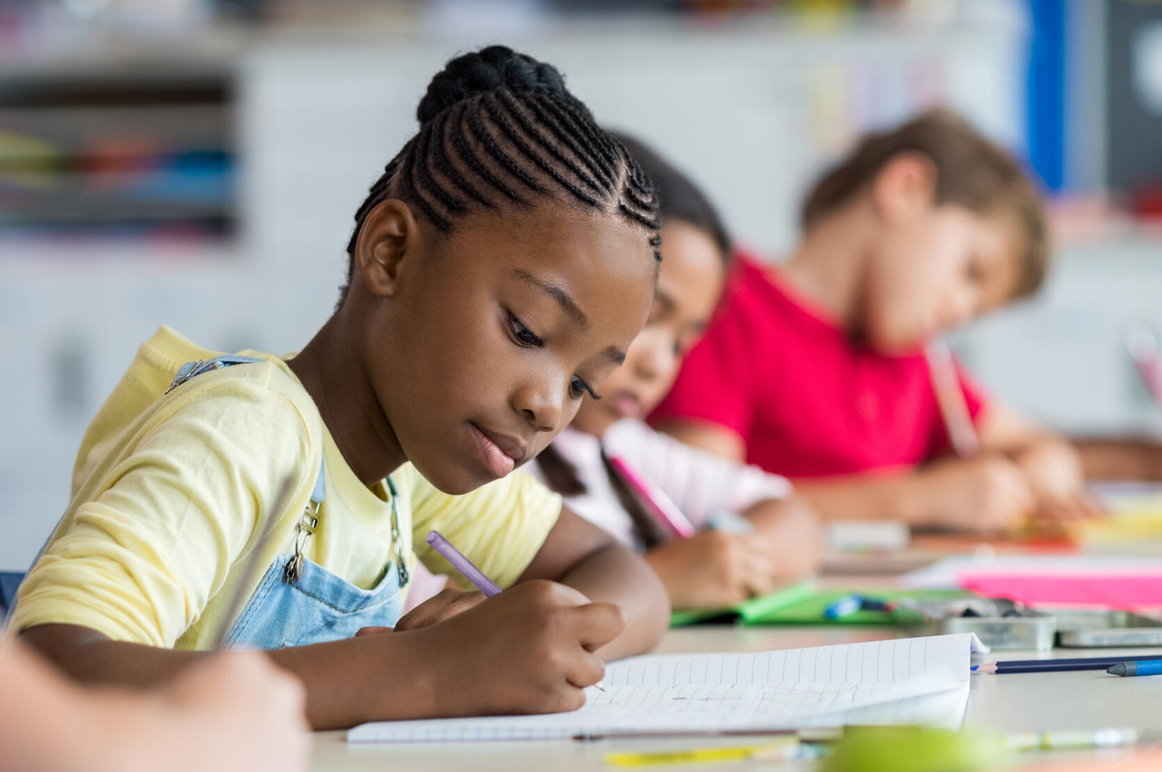 Young black girl, likely in middle school, working on a writing assignment in her classroom.