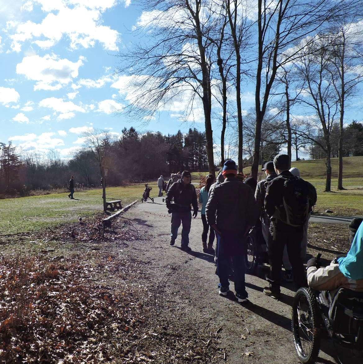 A group of hikers sets off on a flat trail. One of the hikers is using a wheelchair.