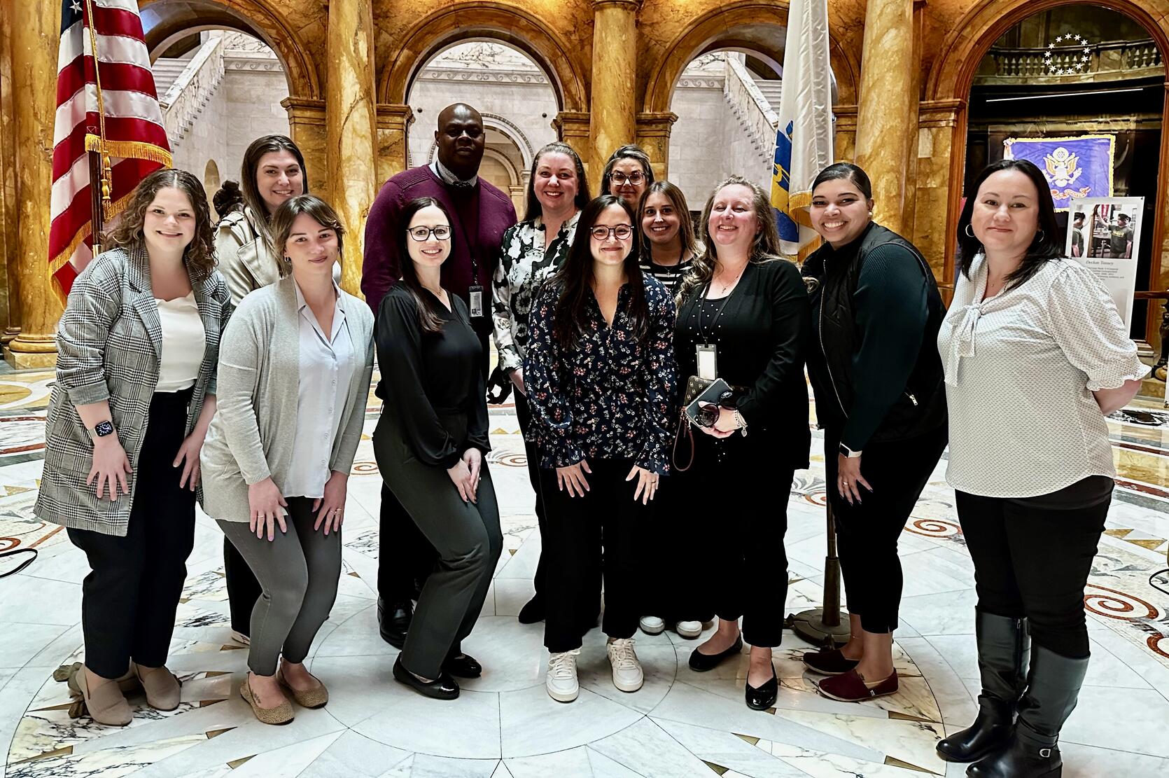 A group poses for a picture in a large, marble atrium. 