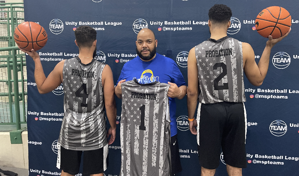 Three men stand in front of a step and repeat, two holding basketballs and the one with a jersey that says "probation."