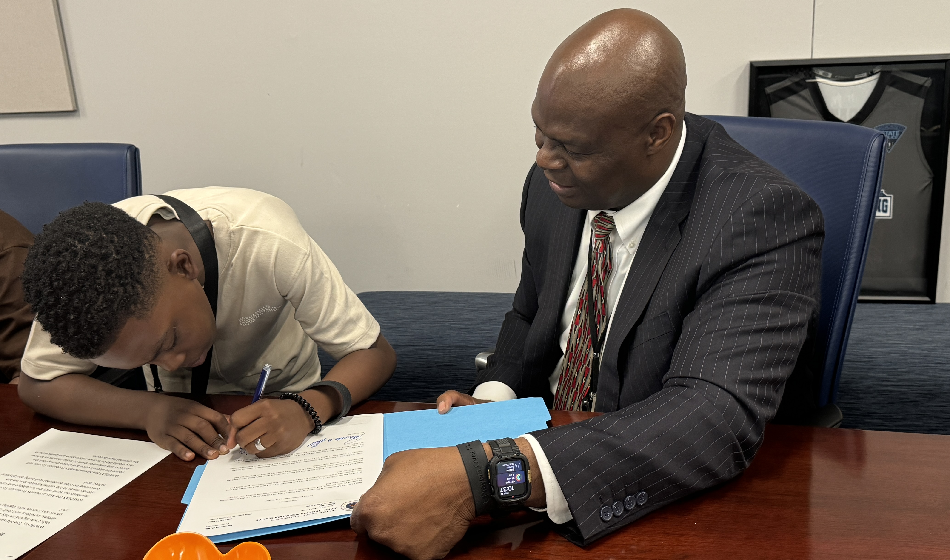 A man holds a folder open as a boy signs a paper