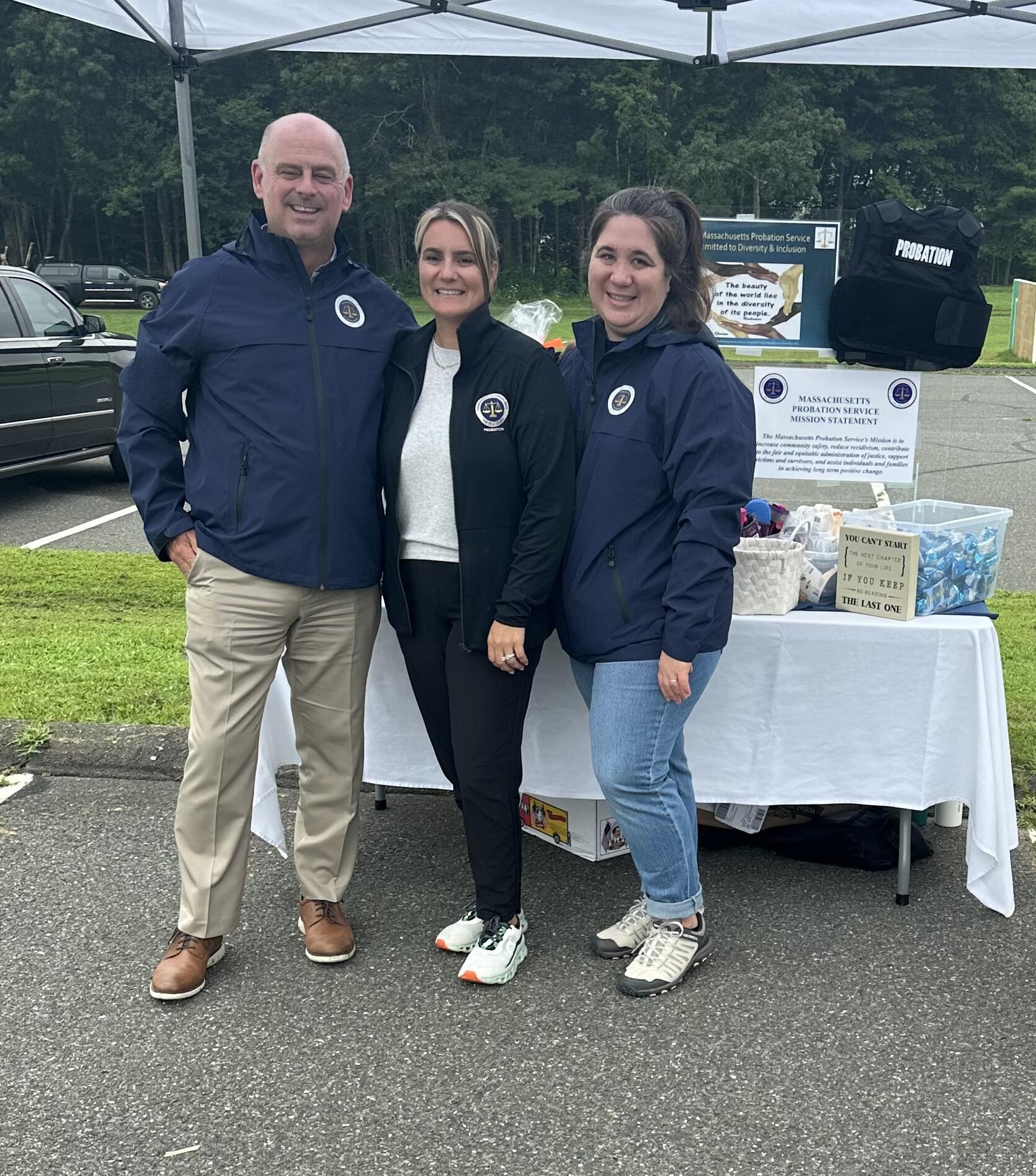 Three members of Eastern Hampshire probation staff standing in front of a table of giveaways for National Night Out.