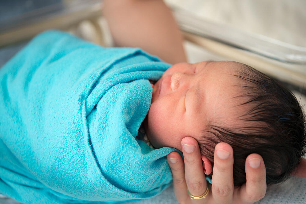 Newborn baby  wrapped in swaddle being held by a nurse.