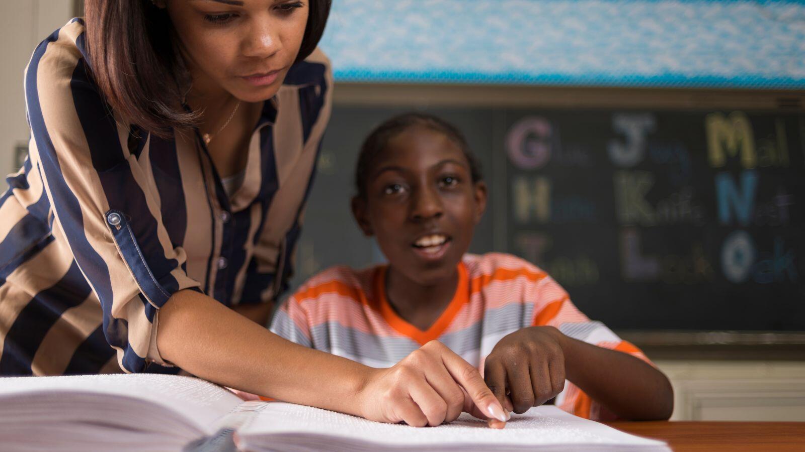 Instructor teaching a young student braille in a classroom