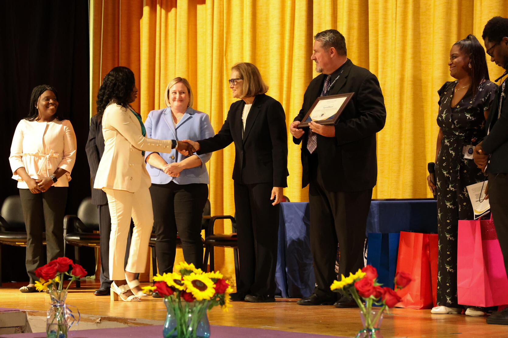 Secretary Walsh shakes the hand of a female participant at the Department of Developmental Services graduation ceremony as other people on stage look on.