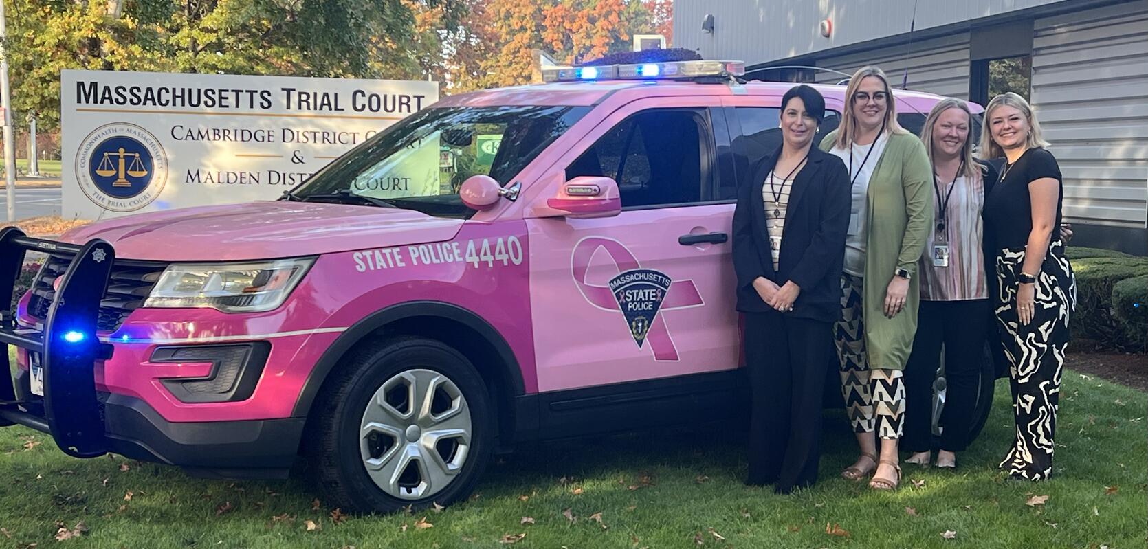 Pink state police SUV with five people standing beside it in front of the Massachusetts Trial Court sign.