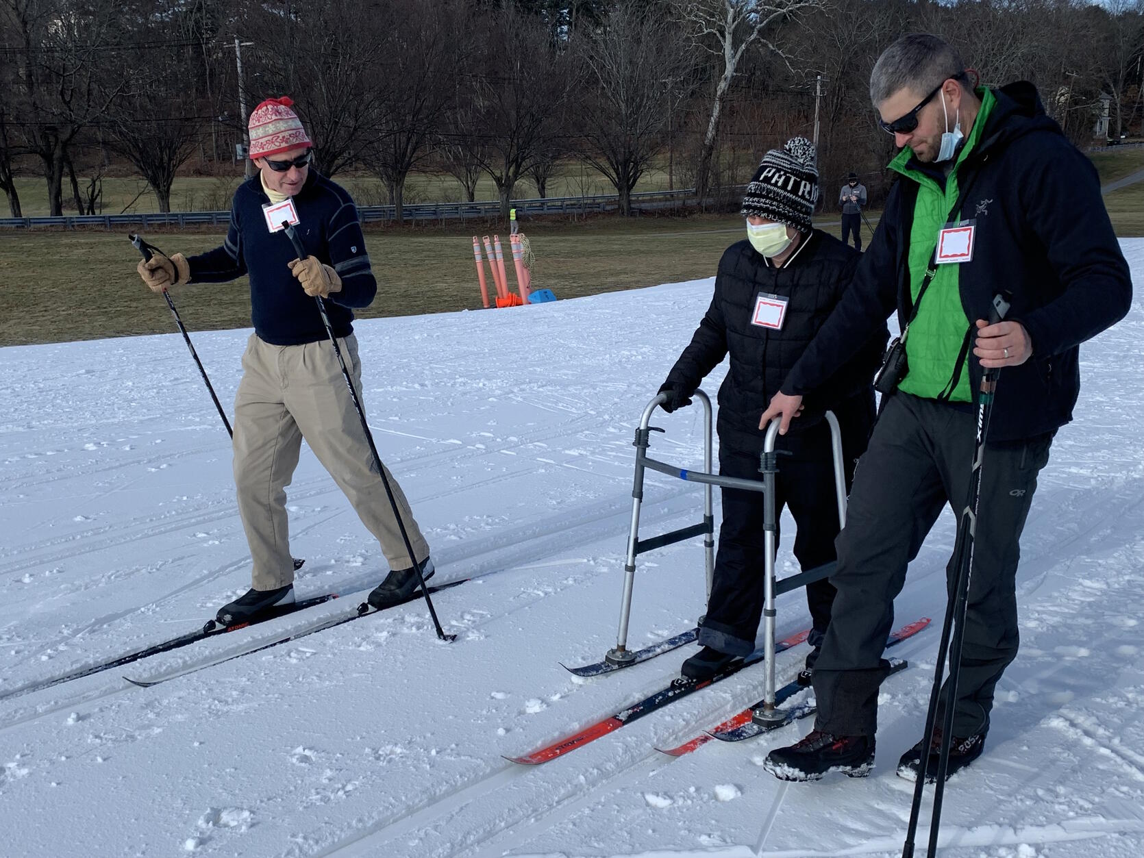 A skier using a walker, assisted by staff.