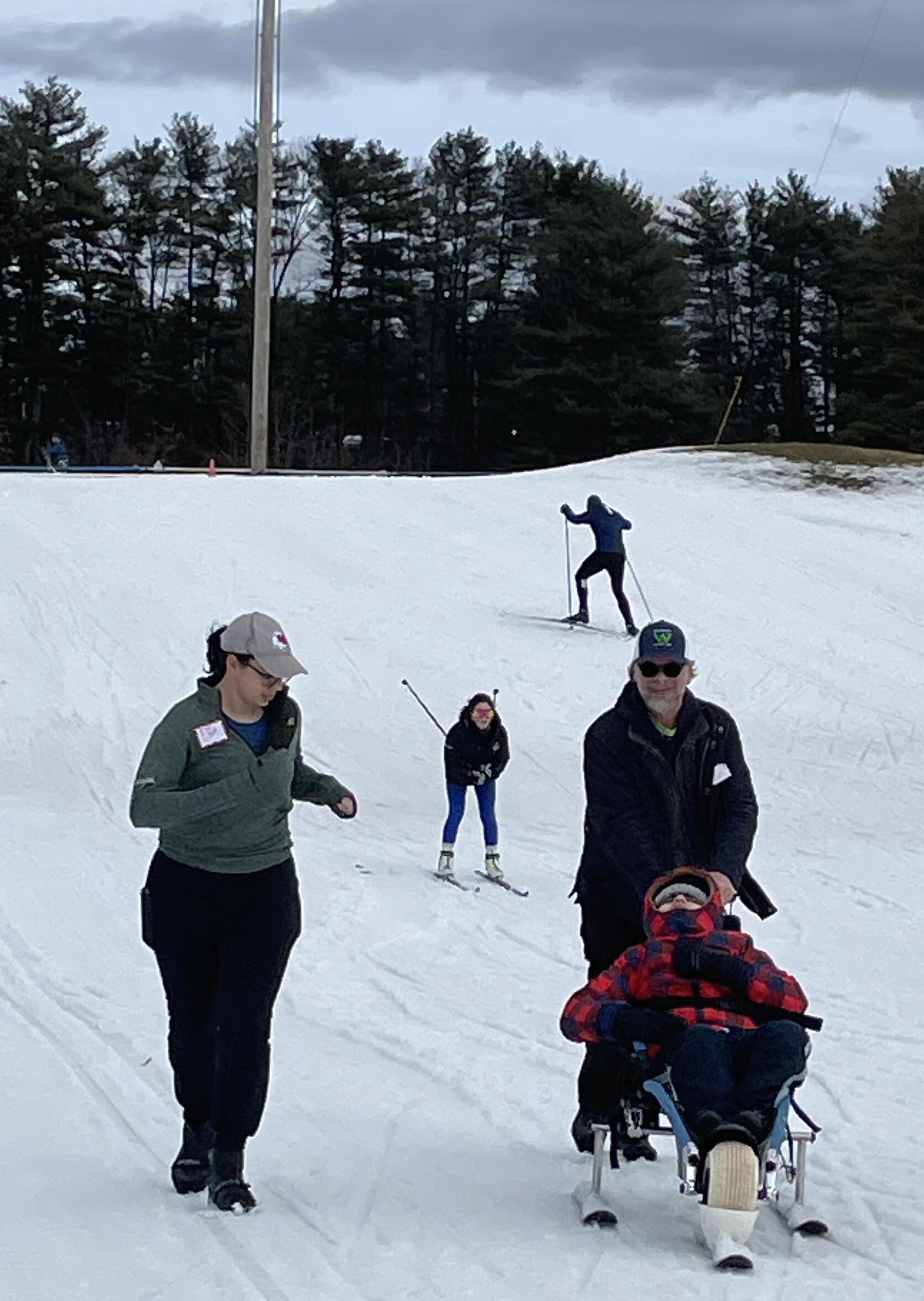 A sit skier is pushed down a gentle hill.