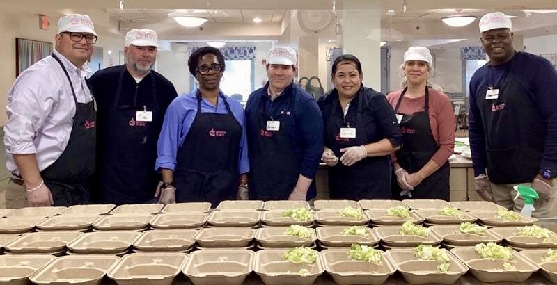 MPS leadership team in aprons and hair nets pose in front of open food containers.