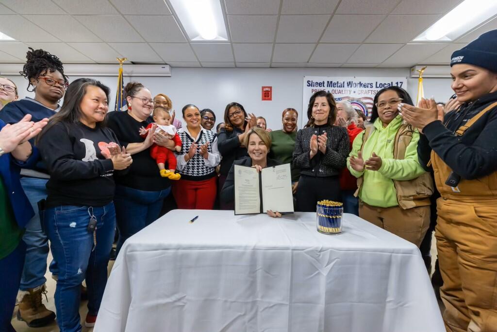 Governor holding a signed executive order in front of a table and with a crowd of people