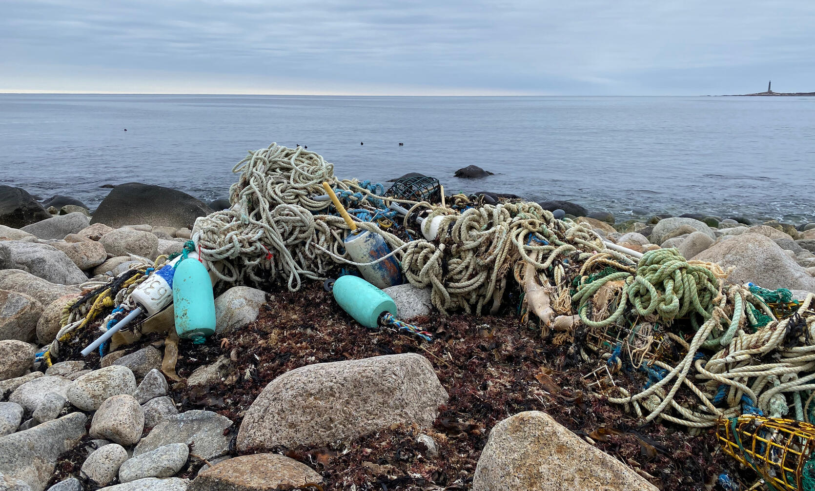 A tangled mass of derelict fishing gear and other marine debris on a rocky ocean shore.