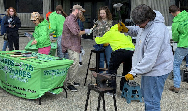 A group of people working at an outdoor event, using a hammer and anvil in front of a building.
