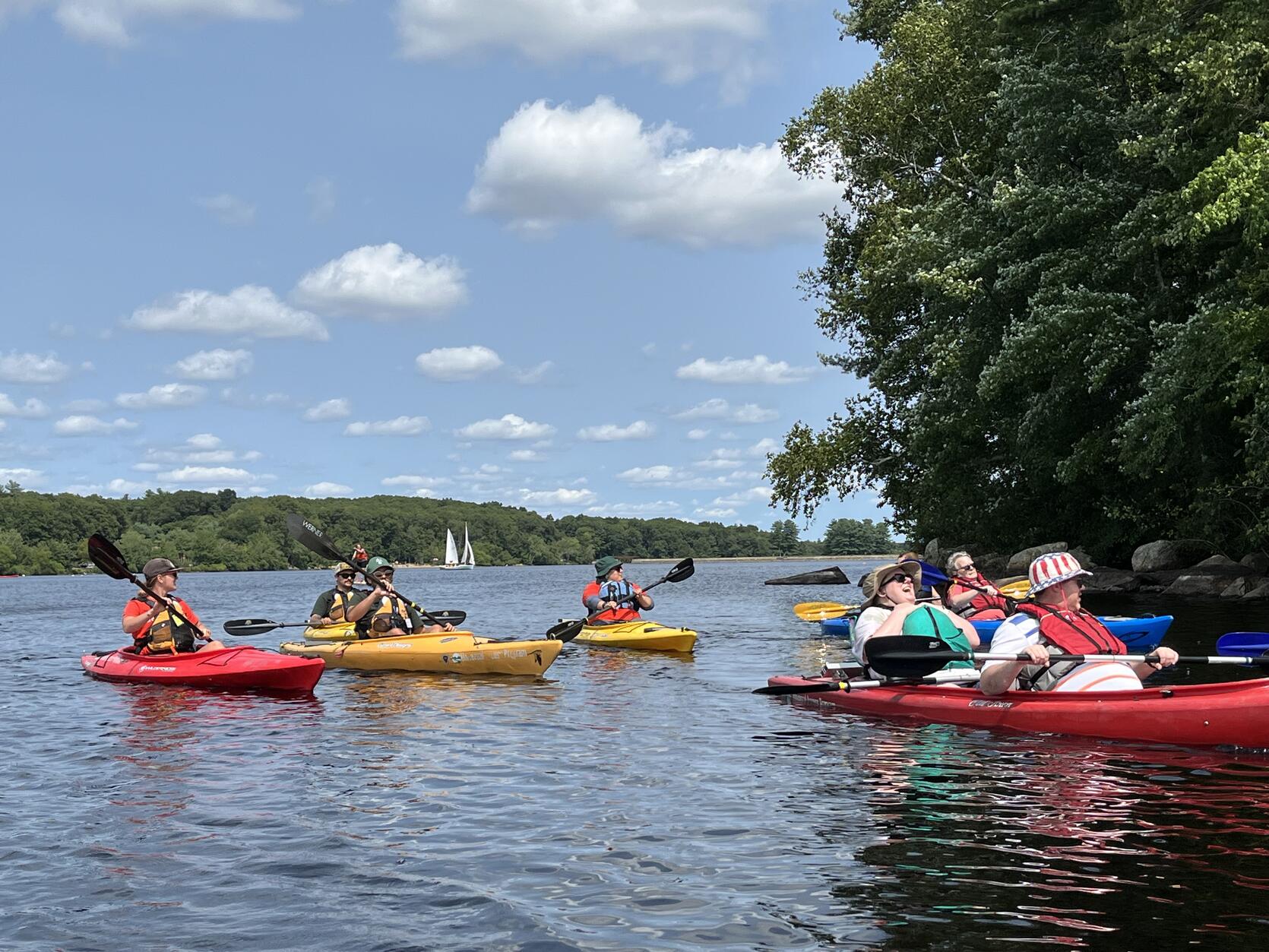 A group of people are paddling on a reservoir in single and tandem kayaks.
