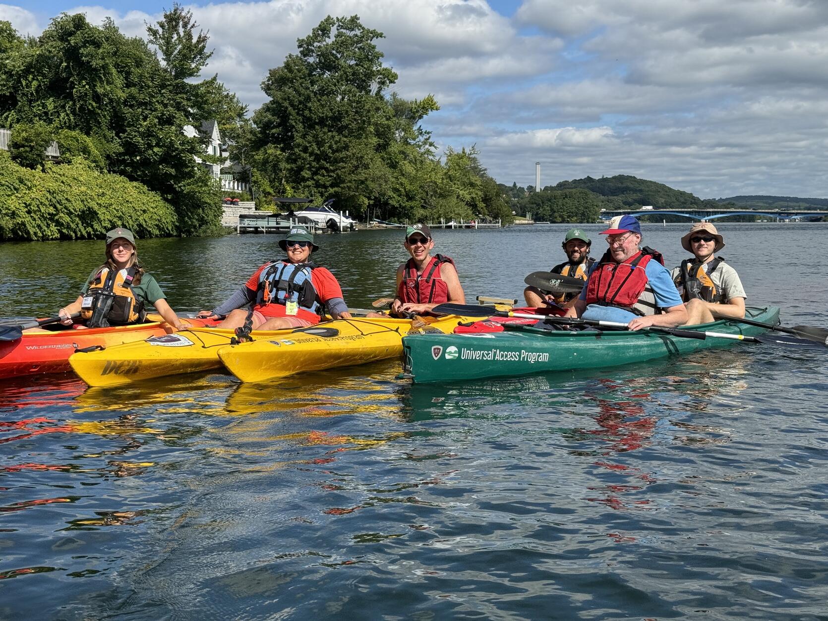 Group of people in single and tandem kayaks on a lake pose for a photo.