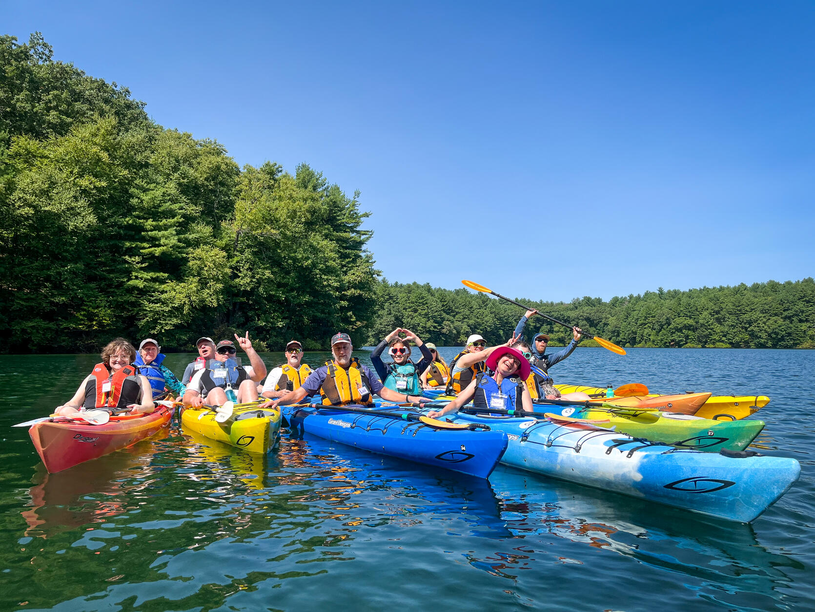 A group of kayakers pose for a picture on a lake in the woods.