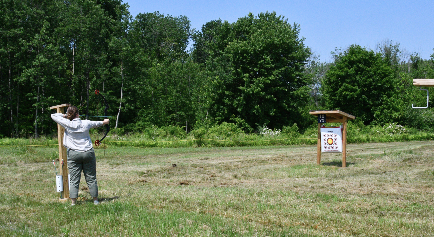 Photograph of a woman aiming a bow and arrow at a target on an outside range