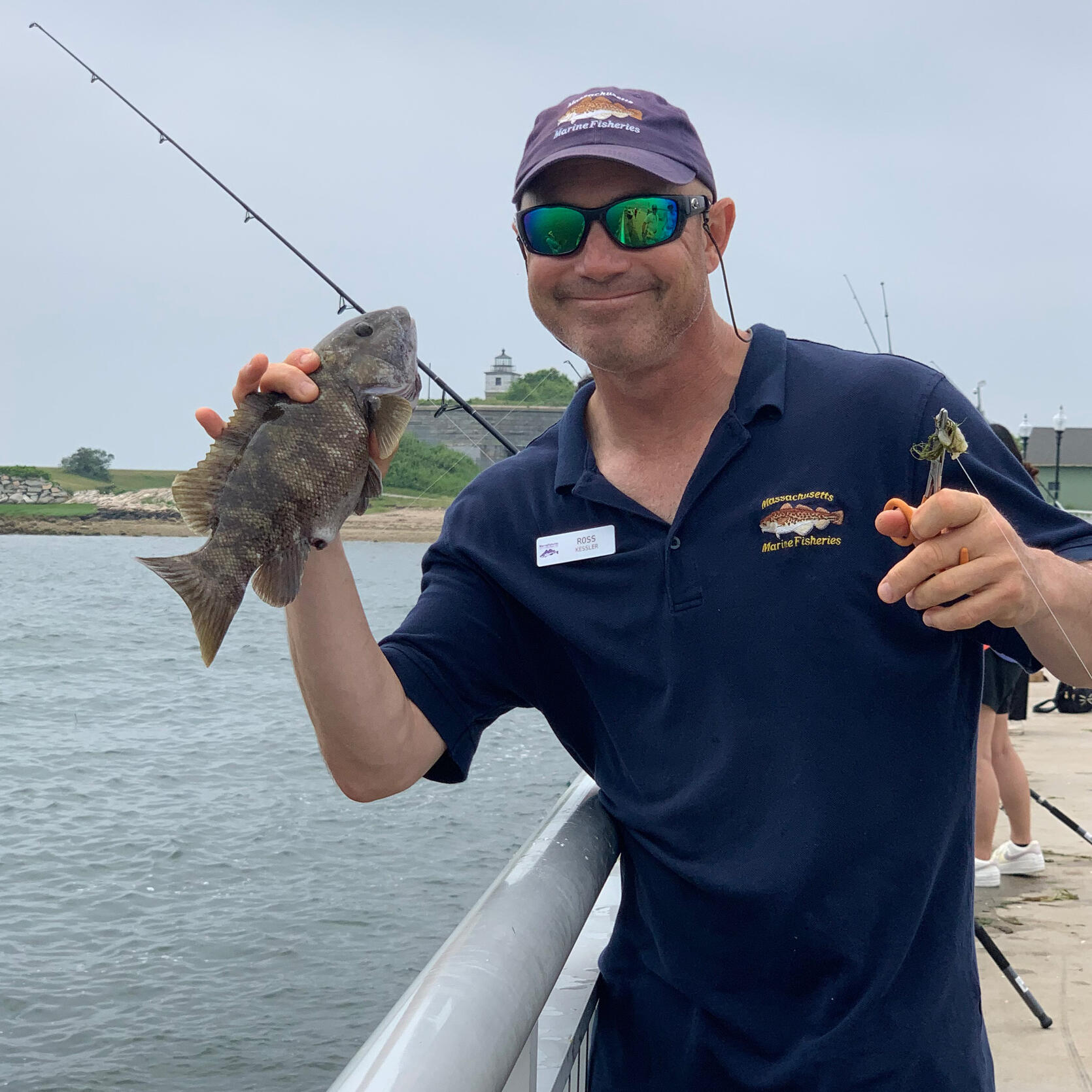A DMF staff member holding up a fish during a fishing clinic on a pier.
