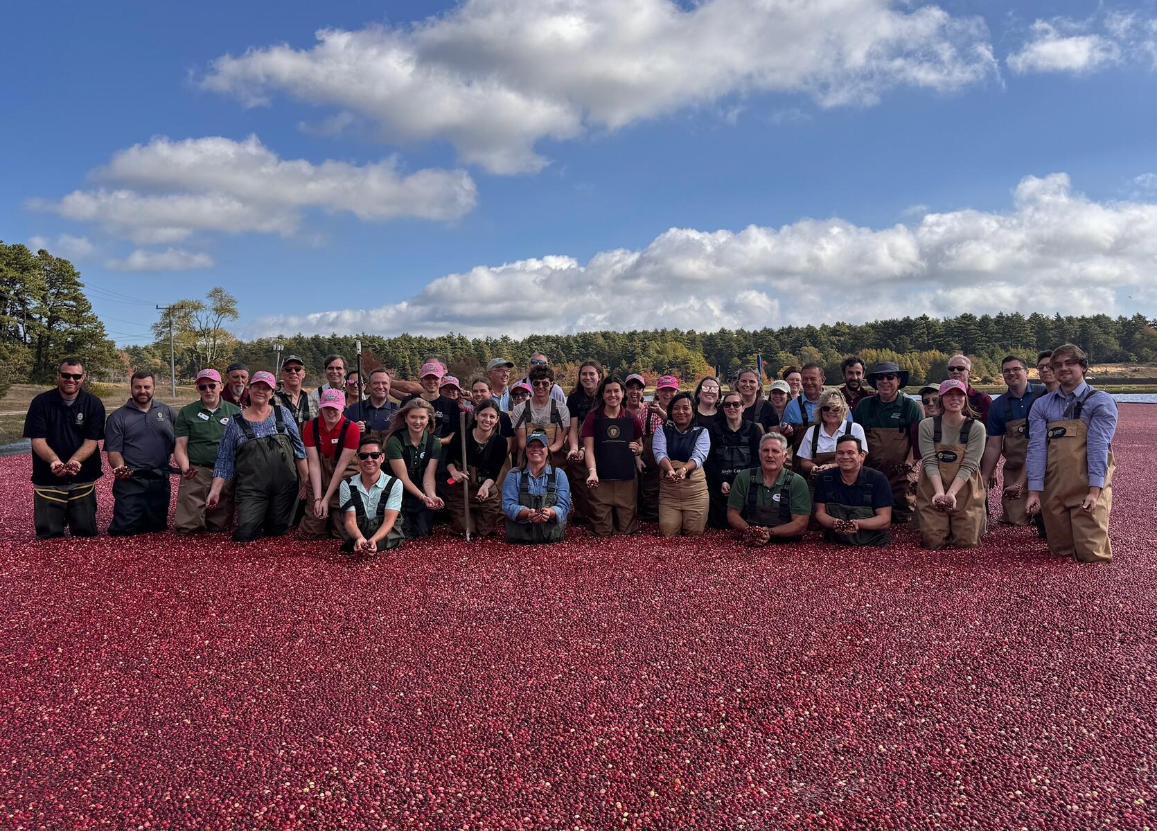 MDAR Commissioner Ashley Randle poses in a cranberry bog alongside a group of people consisting of local cranberry growers, state officials, members of Massachusetts Cranberries, the Agricultural Youth Council, and MDAR staff