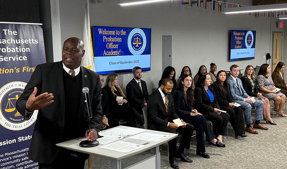 A man speaks at a podium, with seated individuals and a "Probation Officer Academy" welcome screen.