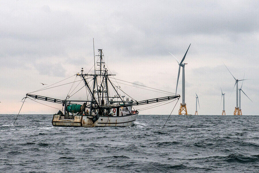 Fishing vessel with offshore wind infrastructure in the distance.