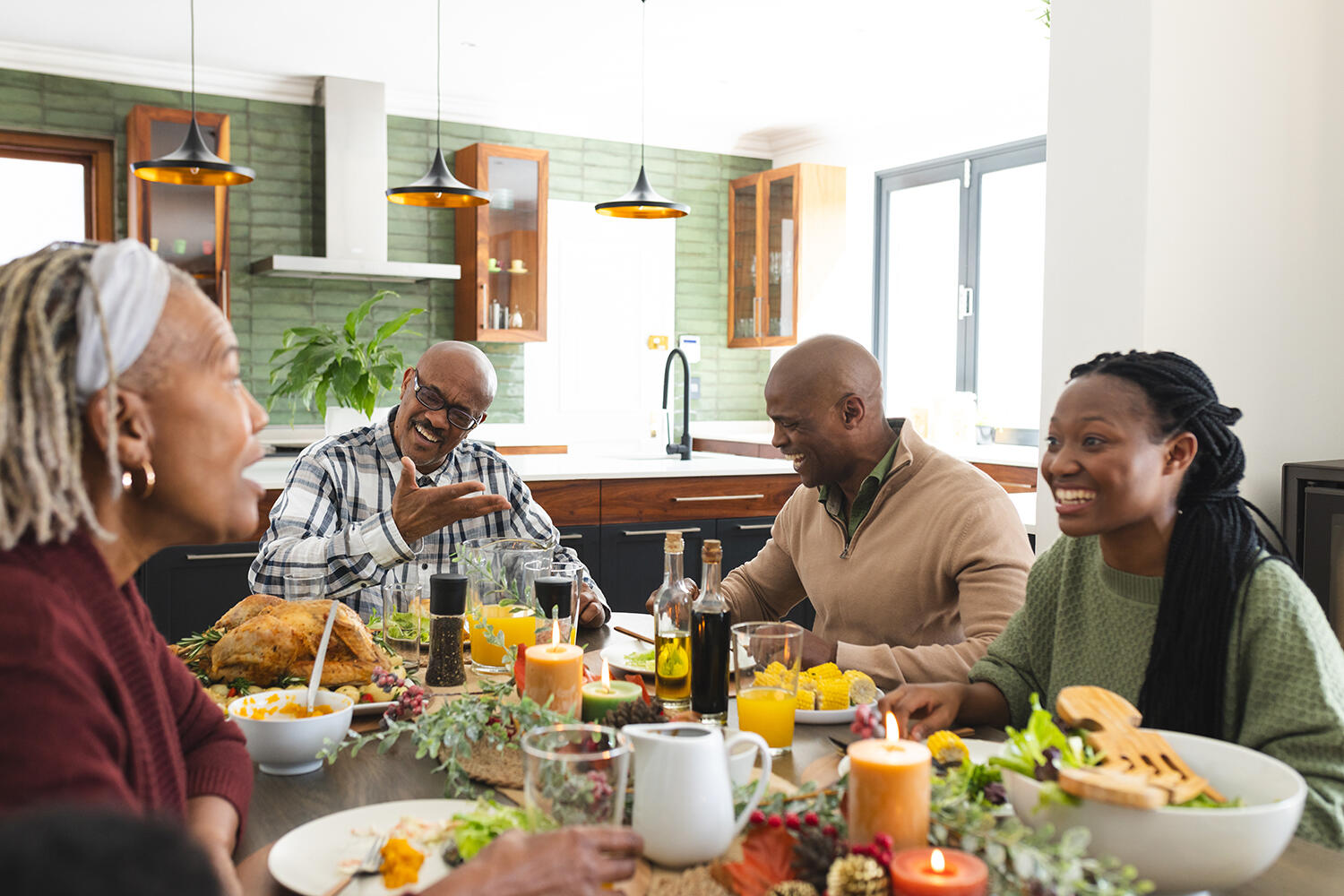 A smiling multigenerational African American family eating a meal at a dinner table while having a conversation.