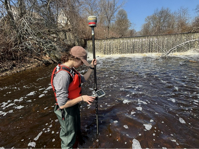 A person measures water quality downstream of a dam in a river.