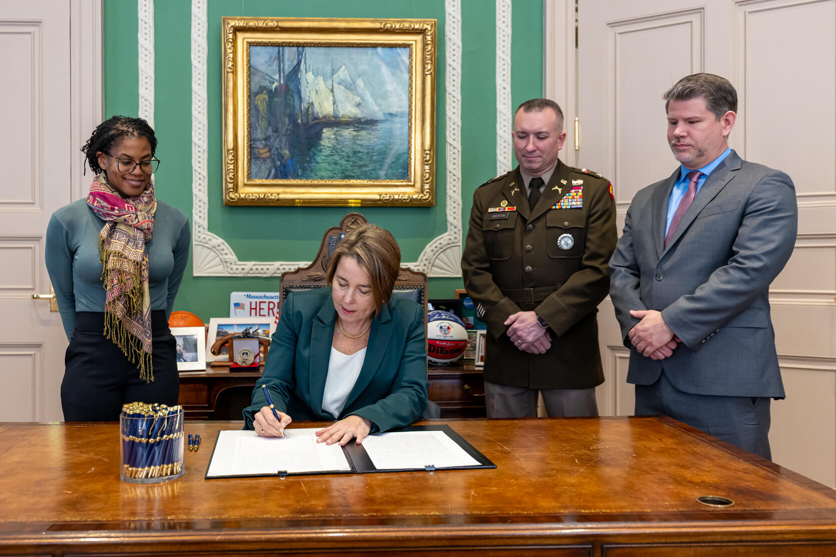 Governor Healey at her desk signing a bill with three people behind her