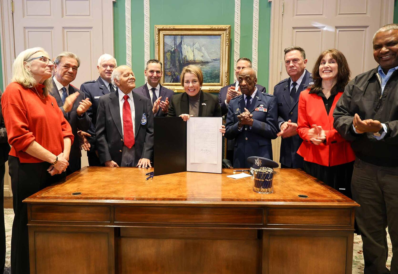 Governor standing behind a desk with a group of people holding up a signed version of the bill