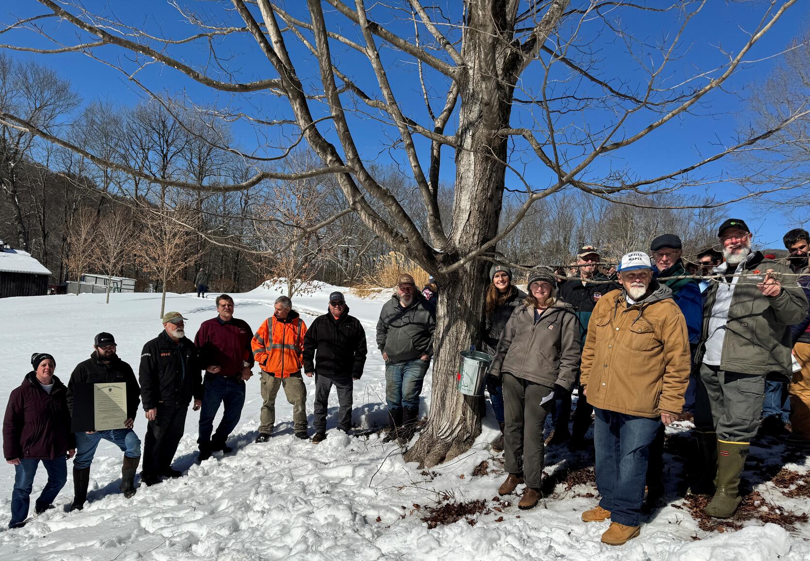 Commissioner Randle taps a Maple Tree and stands with local maple sugar producers