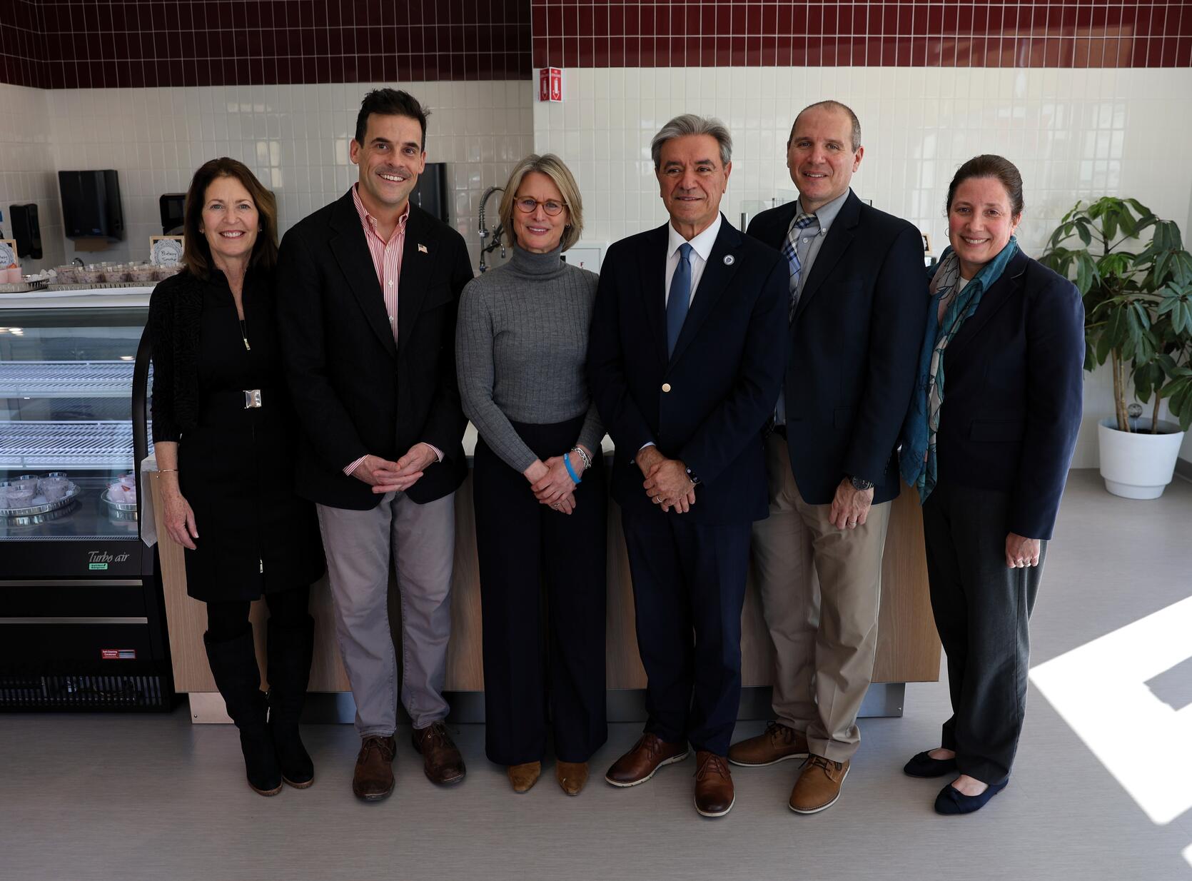 A group of state officials, legislators and advocates, including Acting Education Secretary Amy Kershaw, stand side by side in front of a kitchen counter inside the New Bedford Culinary and Nutrition Center.