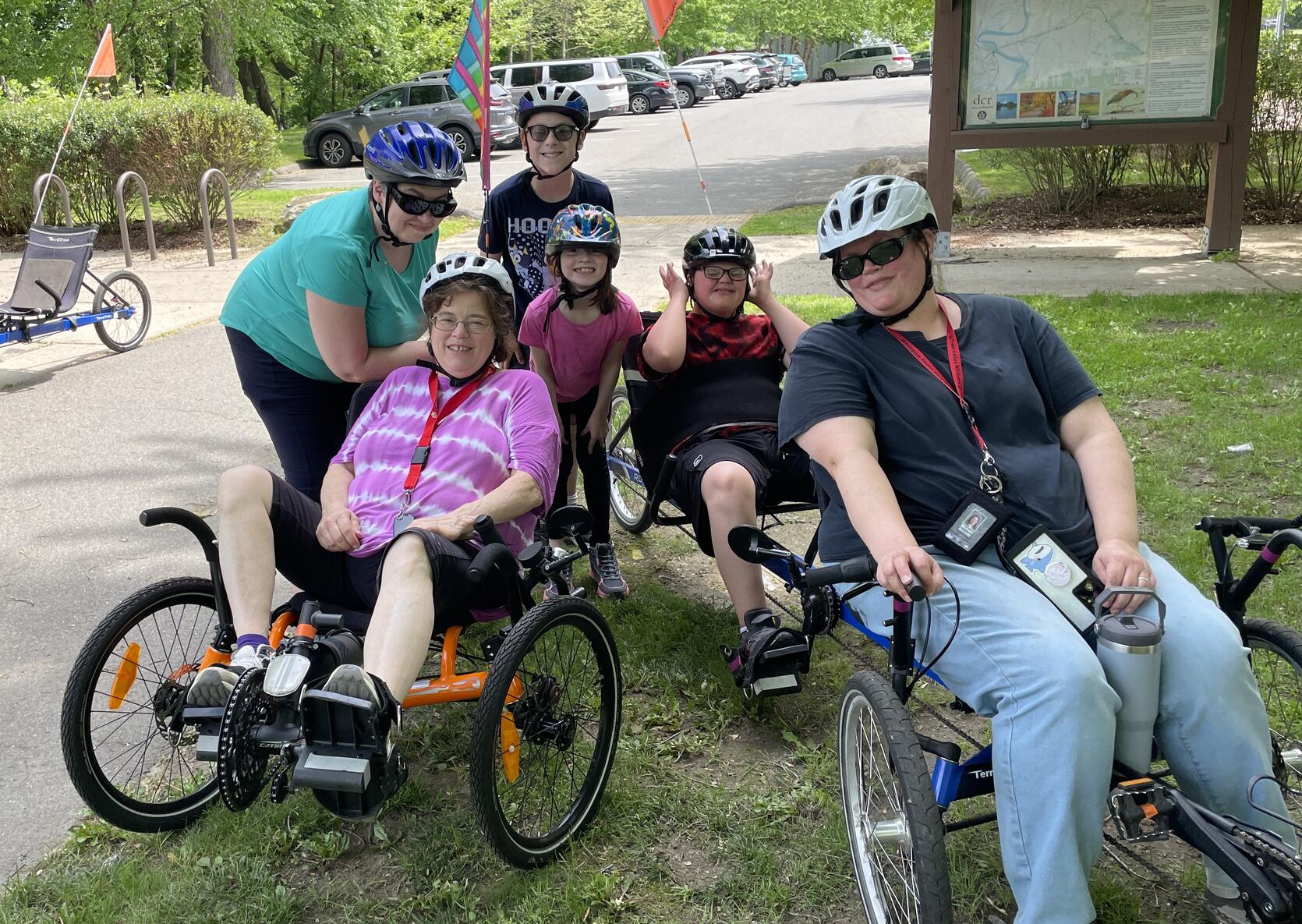 A family riding a variety of recumbent cycles poses for a photo while taking a break along a paved bike path.  