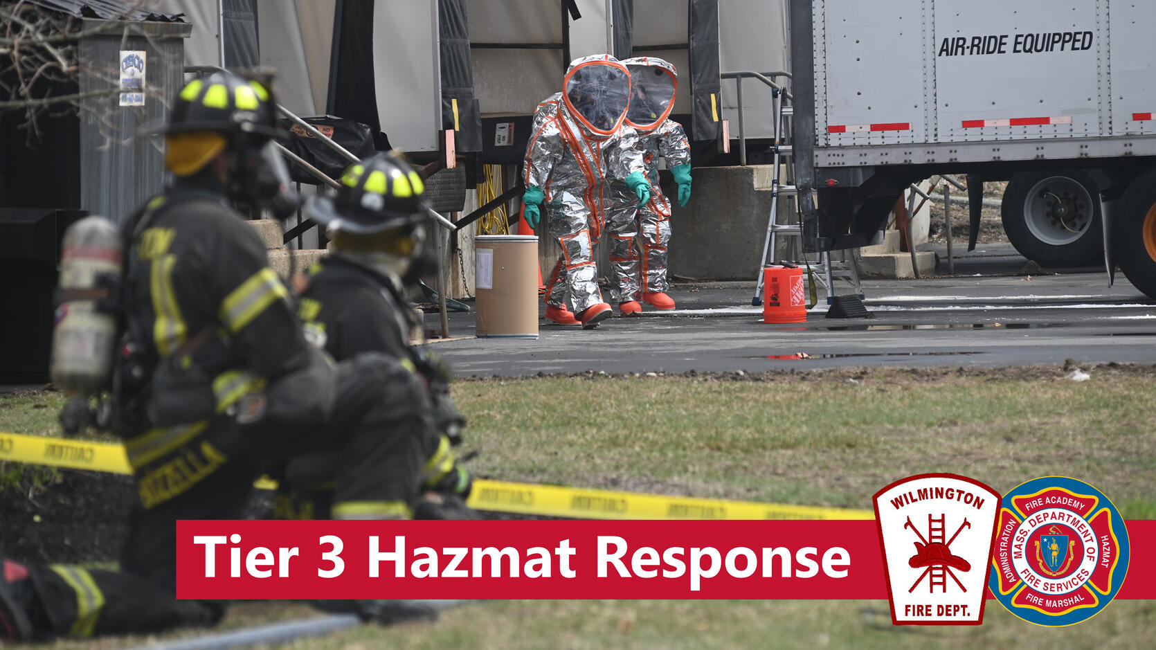 Firefighters stand ready as Hazmat techs work near a tractor trailer, with the words Tier 3 Hazmat Response
