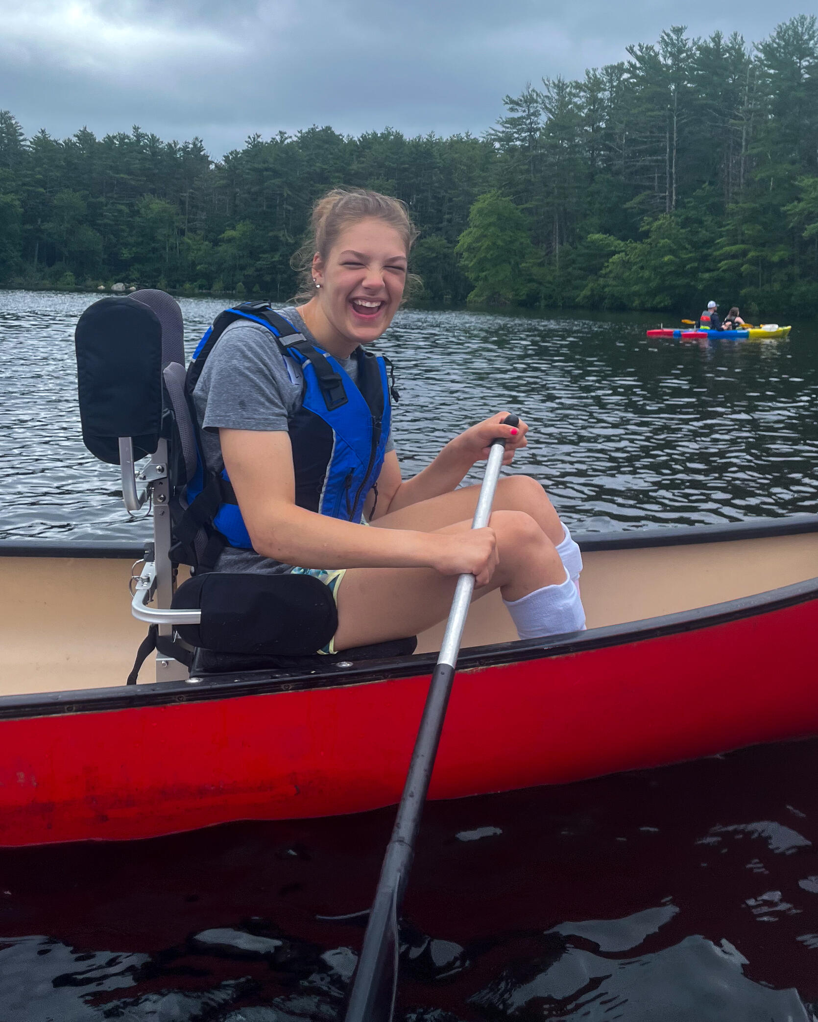 Young person laughs while paddling in a canoe fitted with an adaptive seat. 