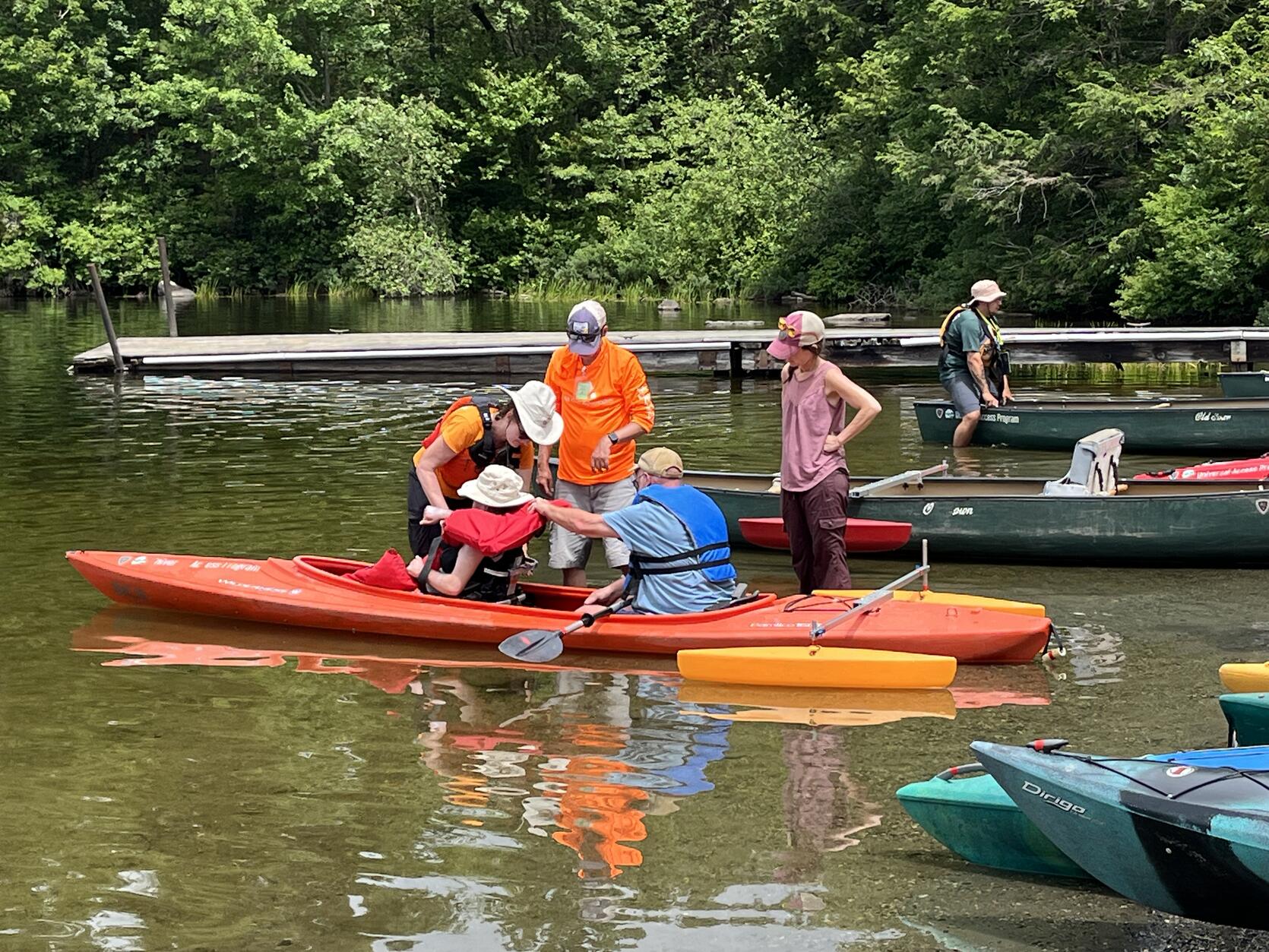 Program staff make adjustments for a person seated in an adaptive seat in a tandem kayak equipped with outriggers. 