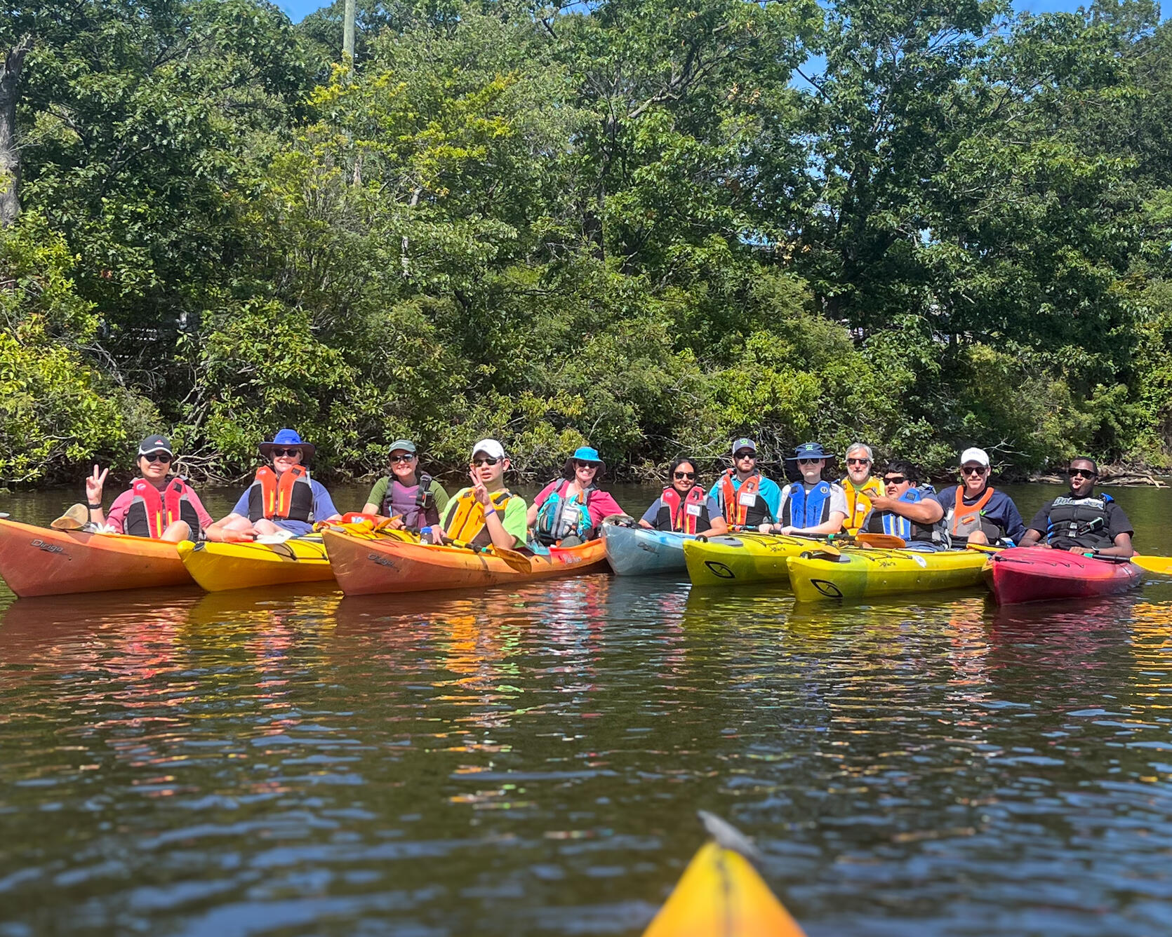 A group of people in tandem kayaks smile for a group photo on the water. 