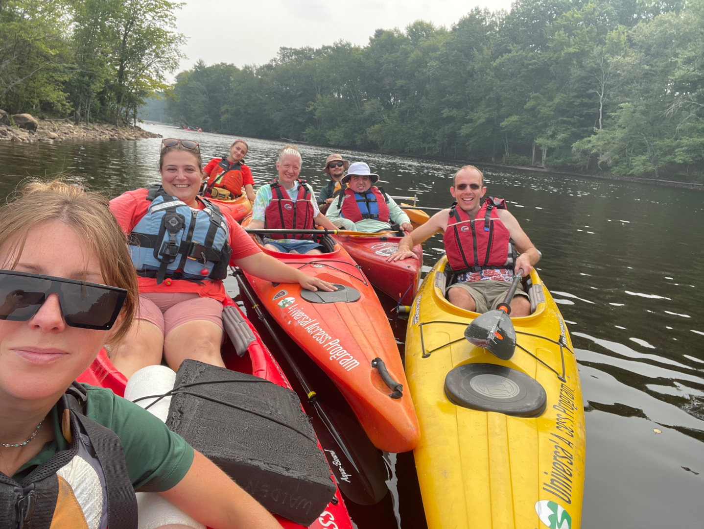 Group of people in single and tandem kayaks smile for a photo on the water. 