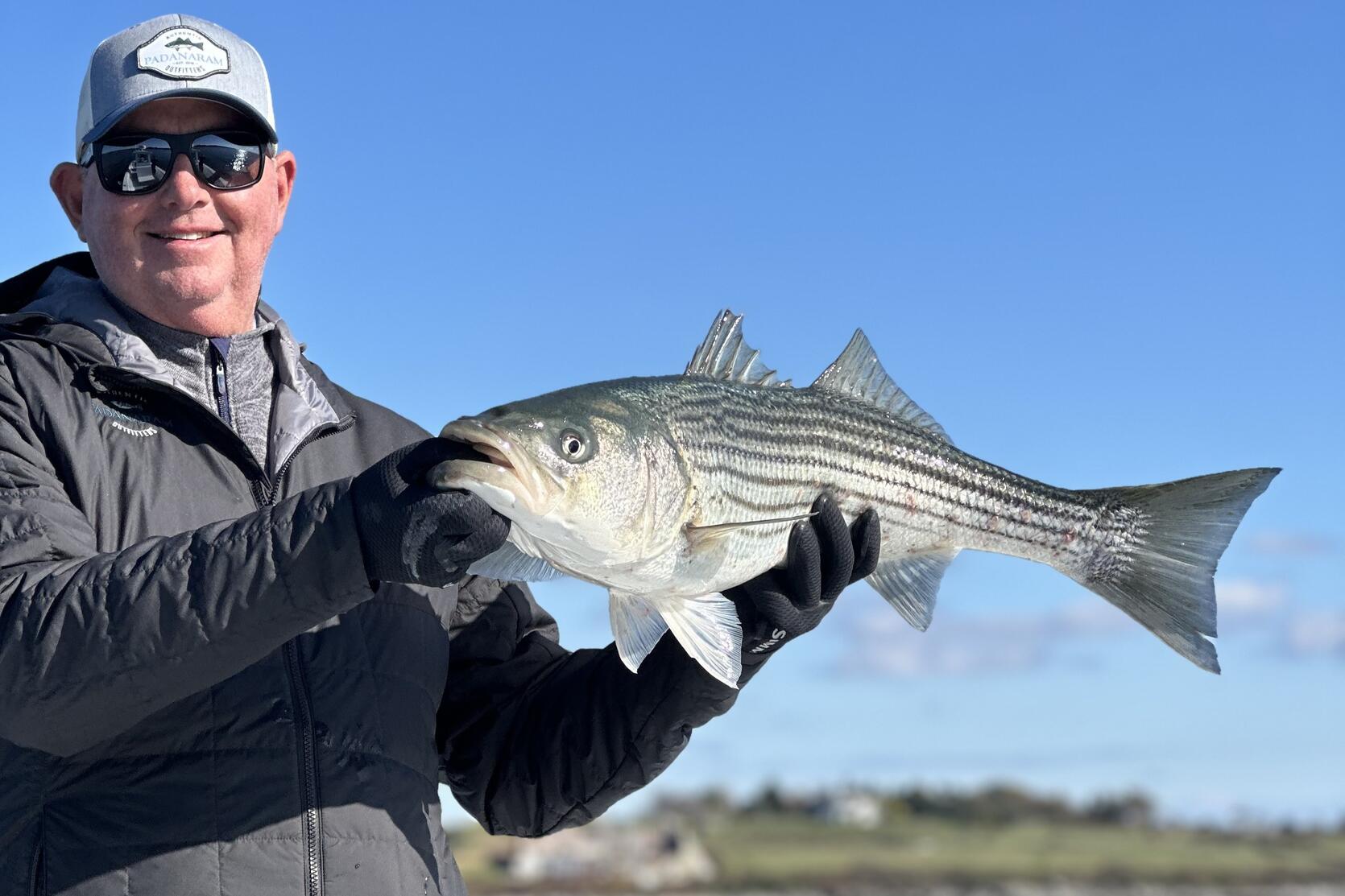 An angler holding up a striped bass that he caught.