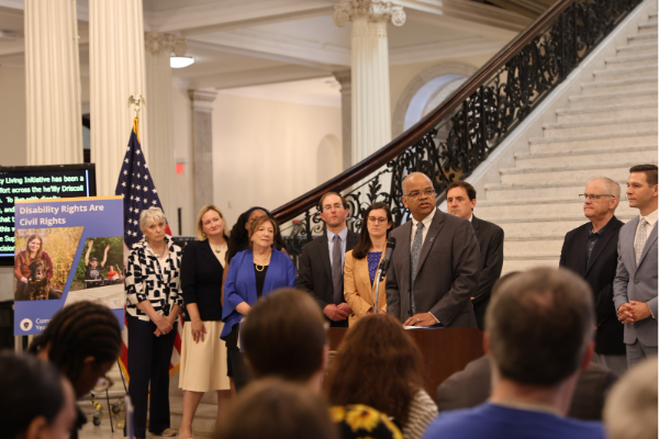 Secretary Mahaniah speaks from a podium at the Grand Staircase on the Community Living Initiative